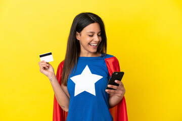 Wall Mural - Super Hero woman isolated on yellow background buying with the mobile with a credit card