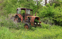 Old Rusty Vintage Abandoned Tractor In A Field Overgrown With Tall Grass.