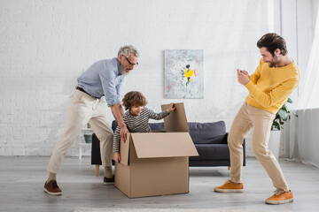 Smiling man taking photo of father and son playing with box