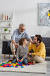 © LIGHTFIELD STUDIOS - Mature man sitting near smiling grandson and son playing building blocks