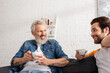 © LIGHTFIELD STUDIOS - Young man talking with smiling father holding cup of coffee in living room