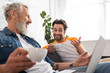 © LIGHTFIELD STUDIOS - Smiling man with coffee pointing at blurred laptop near father at home