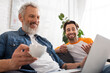 © LIGHTFIELD STUDIOS - Smiling man holding coffee near son and blurred laptop