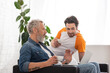 © LIGHTFIELD STUDIOS - Young man talking to father with coffee near laptop in living room