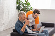© LIGHTFIELD STUDIOS - Excited man with coffee looking at laptop near father on couch