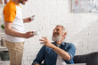 © LIGHTFIELD STUDIOS - Smiling mature man sitting on couch near son with cups of coffee