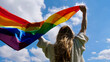 Blonde, lesbian, woman holding a rainbow LGBT gender identity flag on sky background with clouds on a sunny day and celebrating a gay parade