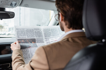 back view of man in suit reading newspaper in car