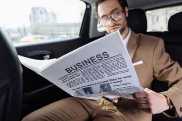 Wall Mural - blurred man in glasses reading business newspaper in car