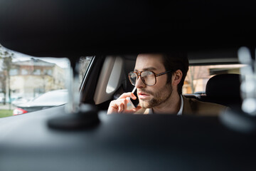 Wall Mural - man in glasses talking on smartphone in car