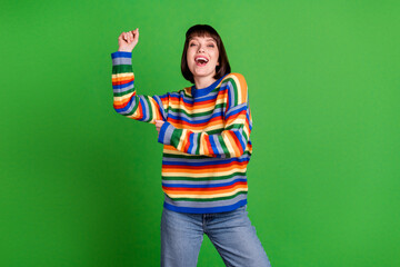 Wall Mural - Photo of cheerful funky young woman dance good mood wear rainbow sweater isolated on green color background