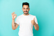 © luismolinero - Young caucasian man isolated on blue background showing ok sign and thumb up gesture