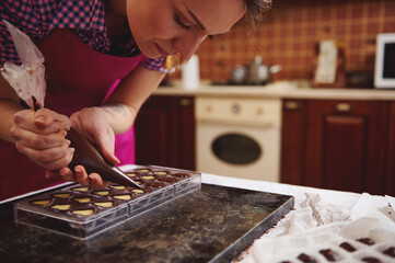 Chef chocolatier squeezing filling of creamy liquid preparing luxury handmade chocolate pralines at home kitchen