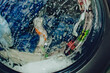 © natavilman - Closeup of washing machine full of dirty clothes. Laundry washing process.