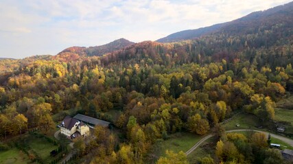 Wall Mural - Aerial view of small shepherd houses on wide meadow between autumn forest in Ukrainian Carpathian mountains at sunset.