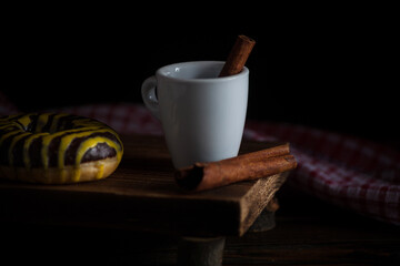 Aromatic morning coffee with cinnamon sticks and fresh donut on a black wooden background. Side view.