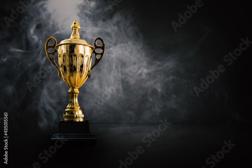 1st champion award, the best prize and winner concept, championship cup or winner trophy on wood table on dark wall and white smoke background