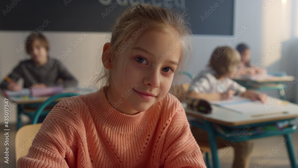 Cute pupil sitting at desk at elementary school. Smiling girl looking ...