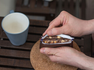 Men's hands break open a package of chocolate. Chocolate with hazelnuts. The opening of the package. Broken chocolate. An empty mug on the table.