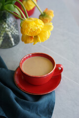 Wall Mural - Bouquet of yellow tulips in a vase and a red cup with coffee on a gray table