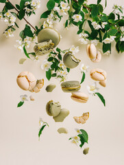 Wall Mural - Sweet pastel French macaroons falling or flying in motion with flowers on beige background. Creative food concept. Trendy patisserie or candy shop aesthetic.