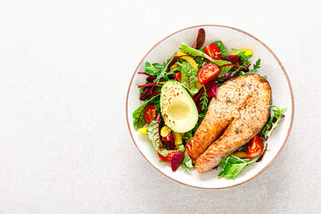 Salmon fish steak grilled, avocado and fresh vegetable salad with tomato, bell pepper and leafy vegetables. Top view