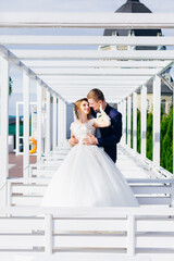 The bride and groom kiss in the park. A couple of newlyweds bride and groom at the wedding in the green forest of nature kiss, against the backdrop of a white arch.