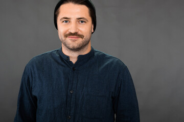 Young hipster guy in knitted hat and casual wear looks at camera with smile isolated on dark background. Concept of self-confident, opportunities, career growth, business education, success, freelance