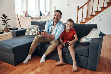 Wall Mural - Happy young father and son playing video games while spending time at home