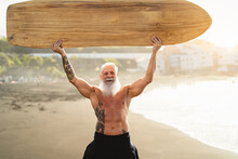 Senior Man Having Fun Surfing During Sunset Time - Fit Retired Male Training With Surfboard On The Beach - Elderly Healthy People Lifestyle And Extreme Sport Concept