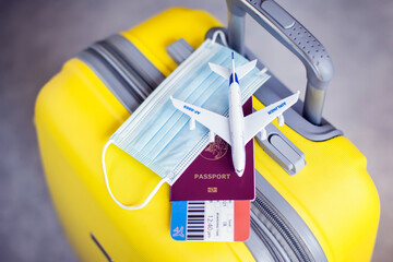 Wall Mural - Traveling during covid-19 pandemic. Luggage, medical mask, passport with ticket and toy plane