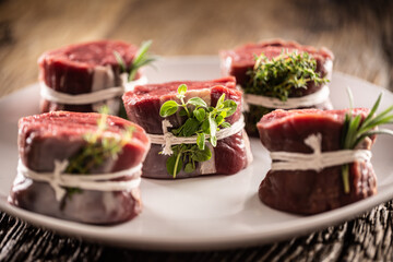 Wall Mural - Raw beef steak cuts on a plate wrapped with strings and fresh herbs