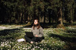 © Girts - Woman with a laptop in the park. Young female sitting in grass with flowers work remotely in nature. Work everywhere travel blogger outdoors. Businesswoman sitting in forest Remote working concept