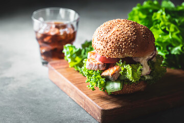 Delicious salmon burger, served on wooden board . Fishburger with fresh salad, fresh vegetables and sauce. Healthy crispy fish burger.