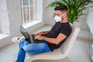 A man in a black T-shirt and mask working remotely from home using a laptop during an epidemic in quarantine