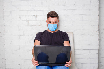 A man in a black T-shirt and mask working remotely from home using a laptop during an epidemic in quarantine