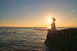 © shodography - Silhouette of Peaceful woman meditating on a rock in the middle of a low wave sea at sunset time. golden hour colorr