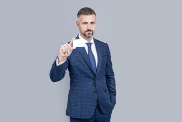 mature man with grizzled hair in suit showing credit or debit card copy space, contact us