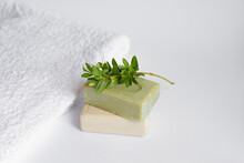 Two Bars Of Natural Green And Ivory Soap With A Green Sprig On The Background Of A White Towel. Concept Eco Organic Natural Cosmetic Products For Skincare. Spa Products