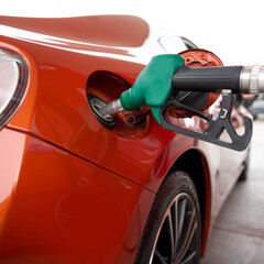 Wall Mural - Green benzene gas pump nozzle filling up red sport car tank. Close up