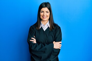 Wall Mural - Young hispanic woman wearing judge uniform happy face smiling with crossed arms looking at the camera. positive person.