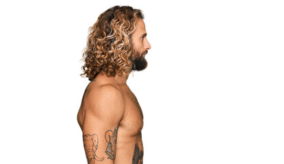 Wall Mural - Handsome man with beard and long hair standing shirtless showing tattoos looking to side, relax profile pose with natural face and confident smile.