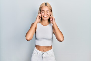 Sticker - Beautiful blonde woman wearing casual style with sleeveless shirt covering ears with fingers with annoyed expression for the noise of loud music. deaf concept.