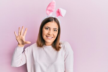 Poster - Young beautiful woman wearing cute easter bunny ears showing and pointing up with fingers number five while smiling confident and happy.