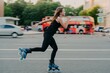© VK Studio - Young fit woman on roller skates with wheels rollerblades during summer day on busy road with transport leads active lifestyle wears black sportsclothes breathes fresh air. Movement concept.
