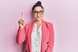 © Krakenimages.com - Beautiful middle eastern woman wearing business jacket and glasses showing and pointing up with finger number one while smiling confident and happy.