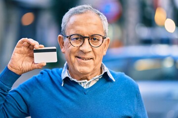 Wall Mural - senior grey-haired man smiling happy holding credit card at the city.