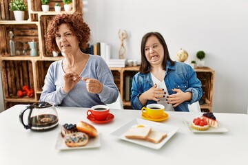 Canvas Print - Family of mother and down syndrome daughter sitting at home eating breakfast disgusted expression, displeased and fearful doing disgust face because aversion reaction. with hands raised