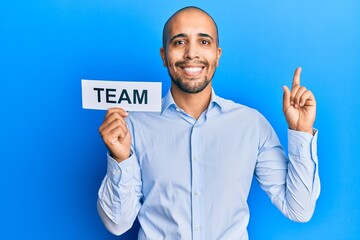 Wall Mural - Hispanic adult business man holding team message on paper smiling happy pointing with hand and finger to the side