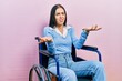 Beautiful woman with blue eyes sitting on wheelchair clueless and confused with open arms, no idea concept.